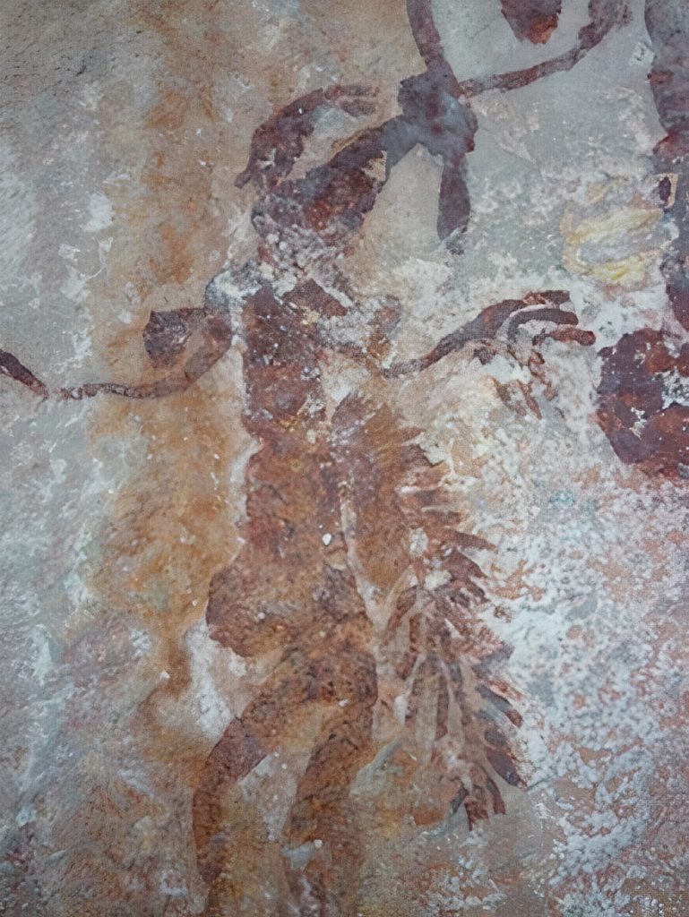 A Kimberley Bent Knee Figure wearing a hanging branch tucked into its belt.