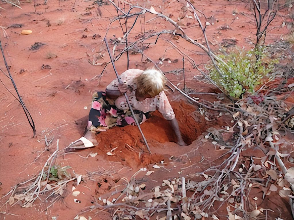 Lena Nambula digs down into the burrow of a sand goanna in the desert region of Central Australia